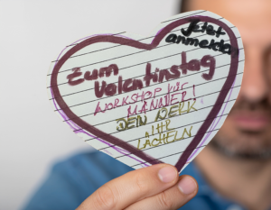 Fotorealistisches Titelbild zum Valentins-Kurs: Ein Mann hält ein handgemachtes Herz im Fokus der Kamera – persönlich, emotional und kreativ. Ein selbstgestaltetes Geschenk von Herzen.